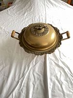 side view of lidded brass serving bowl showing wood handles and ornate rim