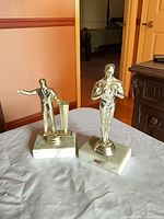 Front view of both gold-tone statuettes on marble bases