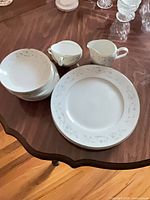 Stacked soup/cereal bowls, creamer, sugar bowl, dinner plates on wood table