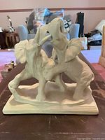Front view of white bisque sculpture showing two elephants rearing and locking trunks