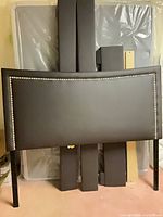 Front view of upholstered headboard with nailhead trim, additional frame pieces stacked behind