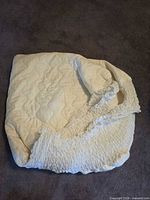 Full view of folded quilted mattress pad showing ruched fitted skirt