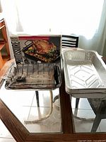 Boxed rotisserie kit with rack, spit rod and stack of aluminum pans on table