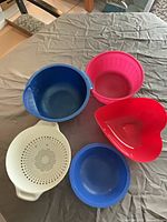 All five pieces displayed: two blue bowls, pink bowl, red heart bowl, white colander