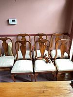 Front view six cherry finish dining chairs with cream seats, detached arms on seat of one chair