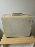 Front view of closed ivory Singer sewing machine case showing handle and staining
