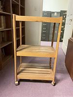 Front view of wooden utility cart showing two slatted shelves and caster wheels