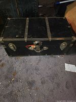 Exterior view of closed black steamer trunk with metal latch and corner hardware visible