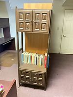 Full view of bookcase front with upper and lower cabinets, open shelf with books for scale