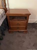 Front view of nightstand beside bed showing missing top drawer, lower drawer, brass pull, bracket feet