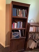Full view of tall brown bookcase with three shelves and lower cabinet