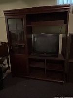 Full front view of mahogany entertainment center showing glass door left, open TV bay right, lower cubbies