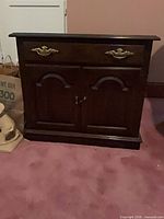 Front view of dark brown cabinet showing drawer, doors, brass hardware