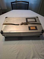 Closed metal storage box showing strap, label holders, and corner protectors