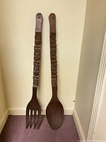 Front view of both carved wood utensils leaning against wall