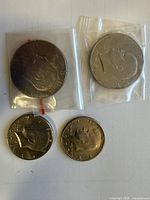 Four coins laid out: two Eisenhower dollars in bags top, two Kennedy half dollars bottom