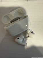 AirPods Pro earbuds and open charging case displayed on light surface