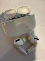 AirPods Pro earbuds positioned in front of open white charging case showing LED indicator