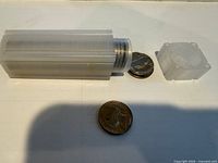 Plastic coin tube with cap and visible stack of nickels plus two loose coins