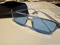front view of VZN sunglasses with blue lenses and case in background