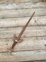 Full view of rusted metal replica sword on wooden surface