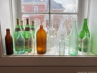 Window ledge with approx. fifteen assorted vintage glass bottles of various colours and shapes