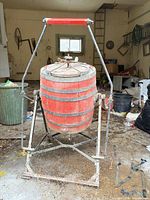 Full view of red wooden barrel butter churn on iron stand
