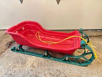 Full view of sled, red body, green runners, yellow rope