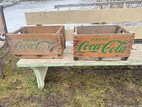 Two Coca-Cola wooden crates side by side showing front green logos