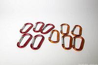 Five red and five orange aluminum carabiners with spring gates laid out on white surface