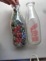 Two Fairfield Hamilton milk bottles, one empty, one filled with assorted marbles, showing red printed graphics