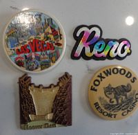 All four souvenir magnets arranged on a surface: Las Vegas round, Reno text, Hoover Dam relief, Foxwoods round.