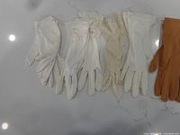 Five pairs gloves laid out: four white/off-white, one brown Kayser