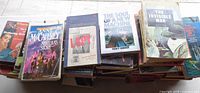 Stack of roughly 30 paperback books; visible titles include Anne McCaffrey "Nerilka's Story", "LSD", Tracy Kidder "The Soul of a New Machine", H. G. Wells "The Invisible Man"
