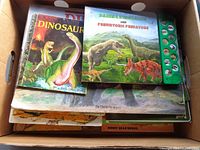 Box containing assorted dinosaur books showing Dinosaurs (pink sauropod) and Daring Dinosaurs board book