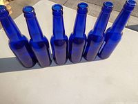 Front view of six cobalt-blue Iceberg beer bottles without visible labels