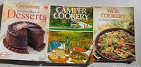 Three cookbooks laid out: desserts, camper cookery, wok cookery