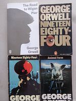 Four George Orwell paperbacks laid out: The Road to Wigan Pier, Nineteen Eighty-Four eye cover, Nineteen Eighty-Four red microphone cover, Animal Farm