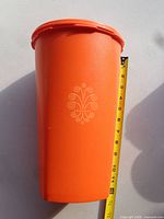 tall orange Tupperware container upright with tape measure indicating height ~10 in