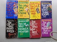 Eight Lilian Jackson Braun The Cat Who series paperback books laid out front covers visible