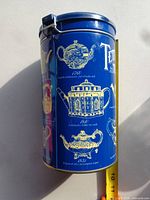 Side view of blue Tetley tea tin showing graphics and clasp lid with measuring tape for scale