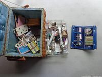Open wicker basket showing blue padded lining and variety of sewing contents with separate blue needle case
