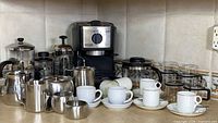 Group shot of espresso machine, French presses, stainless accessories and cups