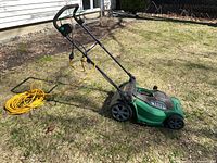side view of green corded electric mower on lawn with attached yellow extension cord