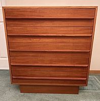 Front view of six-drawer teak dresser showing drawer fronts and plinth base