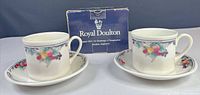 Front view of both teacup and saucer sets with original Royal Doulton box