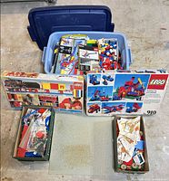 Overview showing tote with loose LEGO pieces, two LEGO boxed sets, grey baseplate and two boxes of parts