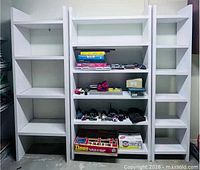 Front view showing all four assembled white bookshelves with some items on shelves for scale