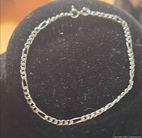 Full view of the sterling silver figaro bracelet displayed on stand
