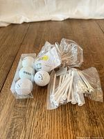 golf balls in clear sleeve, bags of white plastic tees on wooden surface